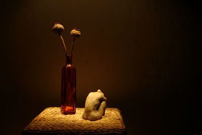 Female figurine by flower vase on side table against wall