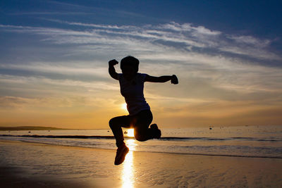 Silhouette mature woman jumping at beach against sky during sunset