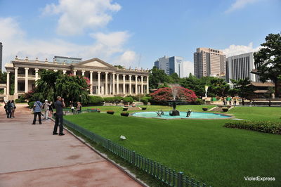 Park by buildings in city against sky