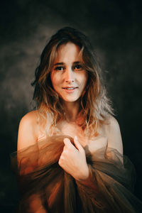 Portrait of young woman standing against black background