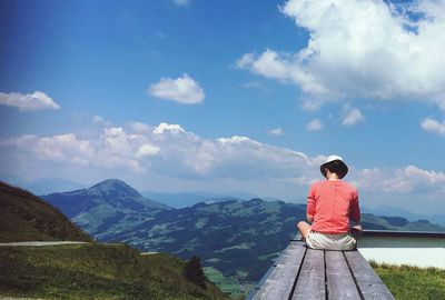 Rear view of man sitting on mountain against sky