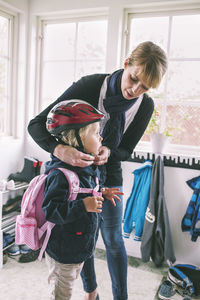 Mother putting bicycle helmet to daughter at home