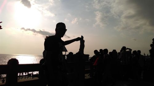 Silhouette people by sea against sky during sunset