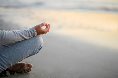 Low section of man meditating while sitting on beach