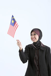 Smiling businesswoman in hijab holding malaysia flag against white background