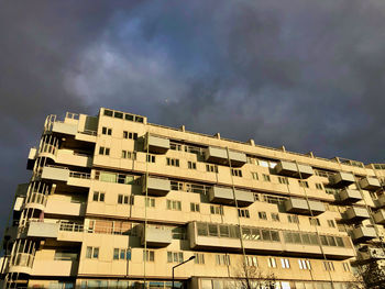 Low angle view of sunlit building against thunderclouds