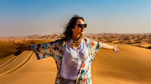 Young woman wearing sunglasses on sand at desert against sky