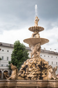 Fountain against cloudy sky in city