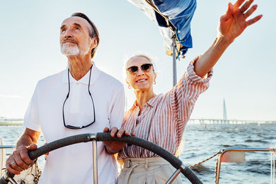 Low angel view of couple standing on sailboat against sea