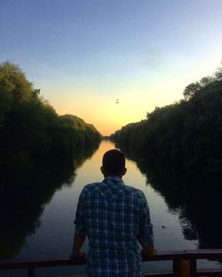 Rear view of man fishing in lake against clear sky