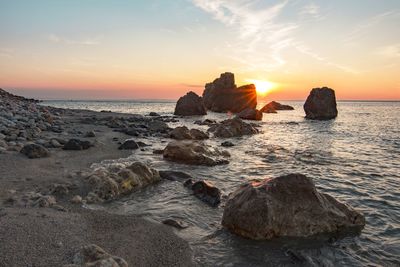 Rocks on sea shore against sky during sunset