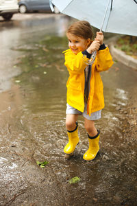 Full length of girl holding umbrella standing in rain