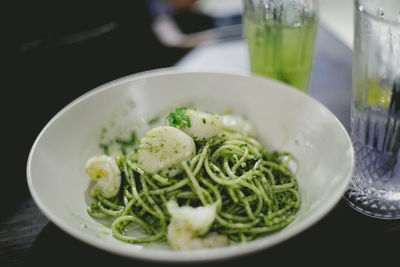 Close-up of spaghetti with vegetable in bowl by drinking glasses on table