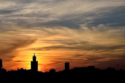 Silhouette buildings against dramatic sky during sunset
