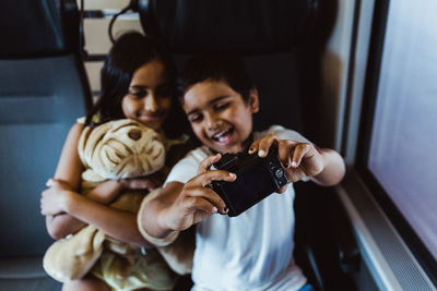 Happy boy taking selfie with sister on camera while traveling in train