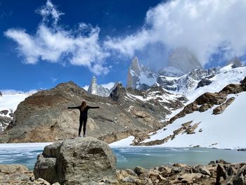 Rear view of person standing on snowcapped mountain against sky