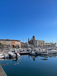 Boats moored in harbor against clear blue sky