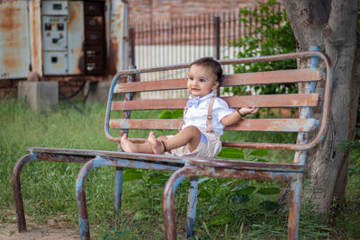 Isolated cute toddler with innocent facial expression sitting at rusty iron bench at outdoor