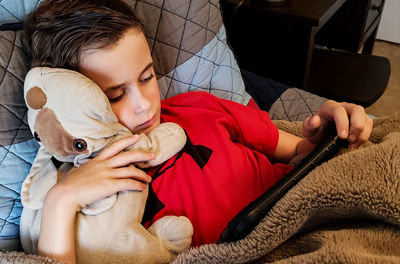 High angle view of boy using phone while sleeping with stuffed toy on bed at home