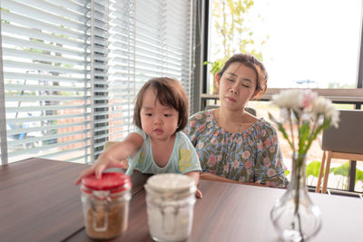 Girl holding container by mother sitting at table in restaurant 