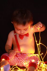 Shirtless boy holding illuminated string lights against black background