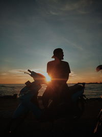 Silhouette man with motor scooter by sea during sunset