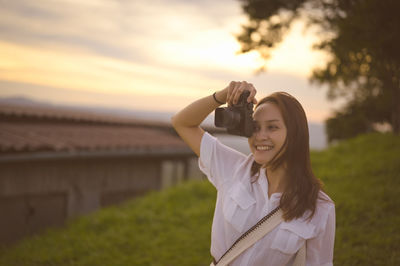 Portrait of young woman standing against sky during sunset