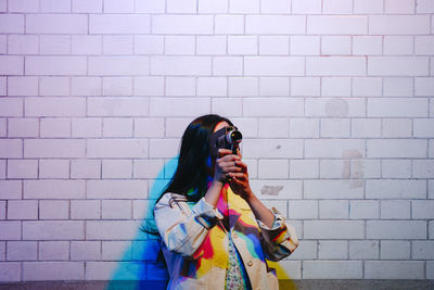 Young woman filming with video camera in front of wall