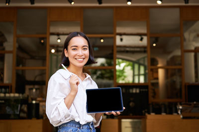 Portrait of young woman using mobile phone while standing in cafe