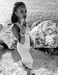 Beautiful young woman holding drink while standing against sea at beach