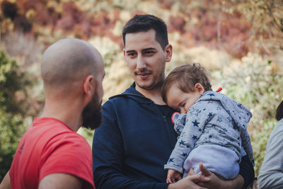 Friend looking at man carrying his sleeping son in forest