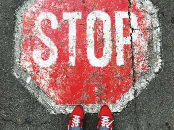 Low section of person standing by stop sign on street