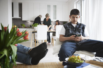 Teenage boy sitting in living room and using phone