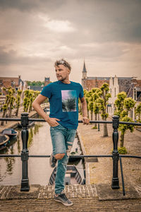 Mid adult man looking away while standing on footbridge against cloudy sky in city during sunset