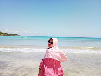 Portrait of woman wearing hijab standing at beach against sky during sunny day