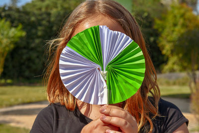 Close-up of girl holding craft product in front of face while standing outdoors