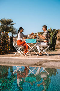 People sitting in swimming pool against clear sky