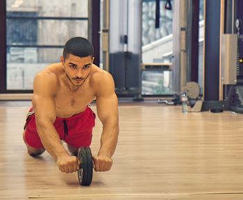 Young man looking away while exercising on hardwood floor at gym