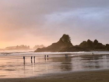 People on beach against sky during sunset