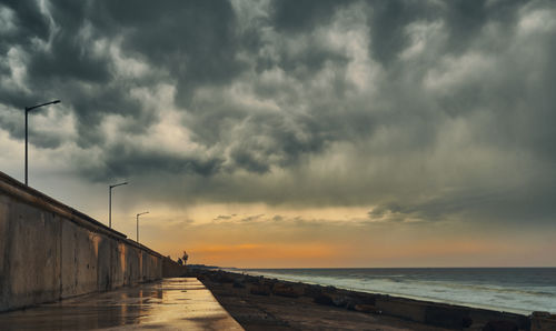 Scenic view of beach against cloudy sky during sunset