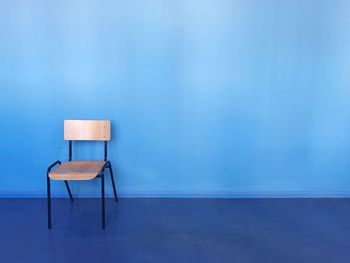 Empty chair on table against blue wall
