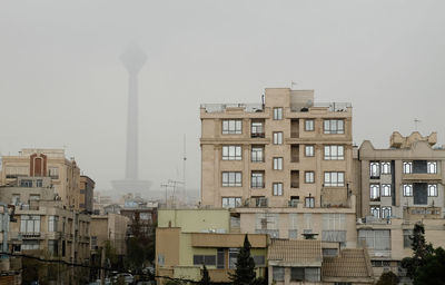 Buildings against milad tower in city during foggy weather