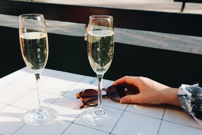Cropped hand of woman holding sunglasses by champagne flutes on table