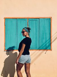 Young woman standing against house during sunny day