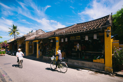 People riding bicycle on street against buildings in city