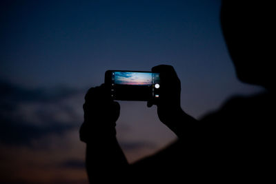 Human hand holding smart phone against sky