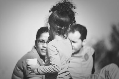 Girl holding disposable cup with parents in background