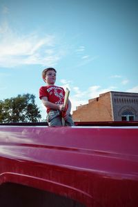 Boy with toy standing on car against sky