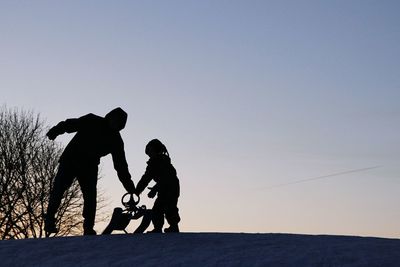 Silhouette father and son with sled against clear sky