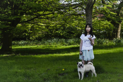Girl with dog standing on grassy field against trees in park